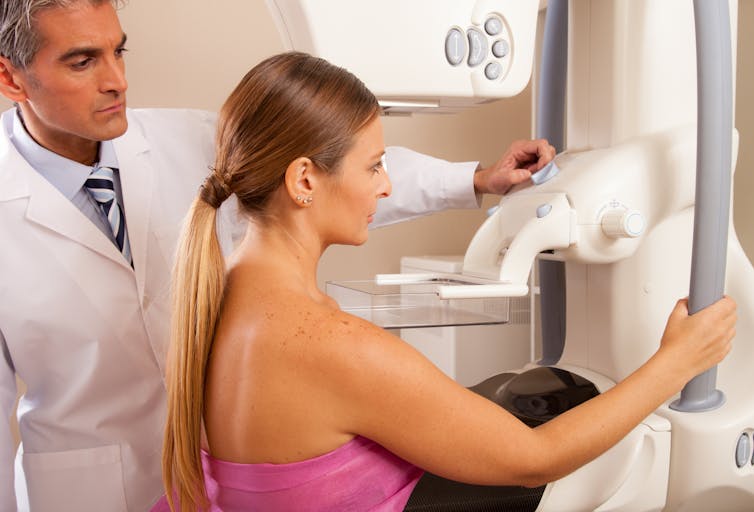 A woman undergoes a breast examination using a machine operated by a male doctor.