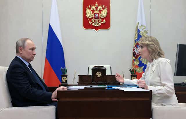 Side view of Vladimir Putin and Russian President Vladimir Putin meets with Russian Presidential Commissioner for Children's Rights Maria Lvova-Belova sitting across a desk from one another in Putin's presidential office