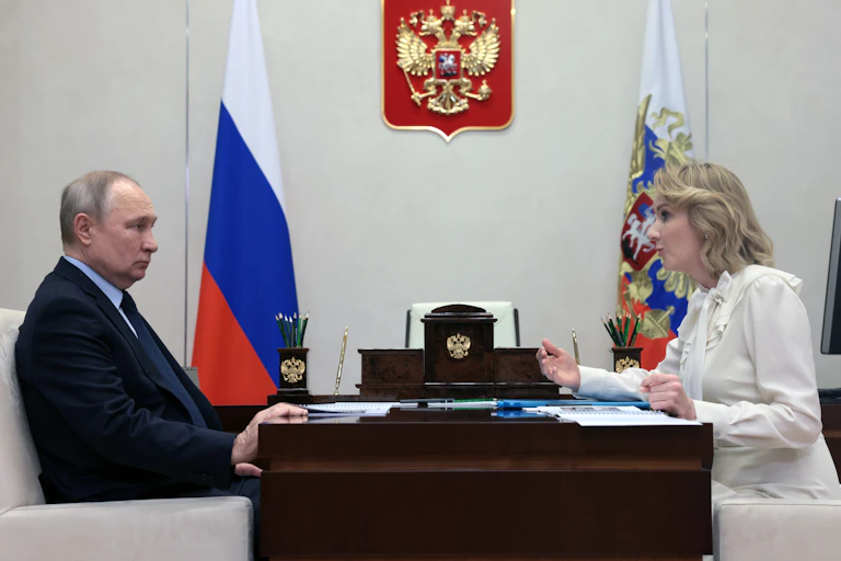 Side view of Vladimir Putin and Russian President Vladimir Putin meets with Russian Presidential Commissioner for Children's Rights Maria Lvova-Belova sitting across a desk from one another in Putin's presidential office