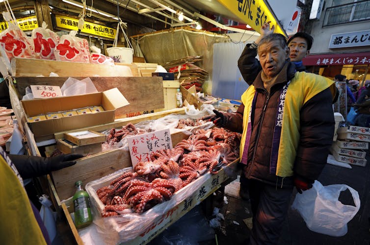 A fishmonger stands in front of a market display stocked with dead octopuses.