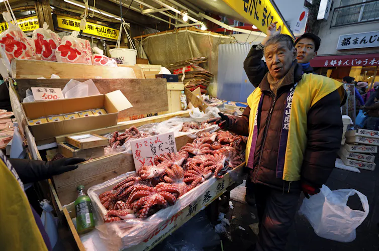 A fishmonger stands in front of a market display stocked with dead octopuses.