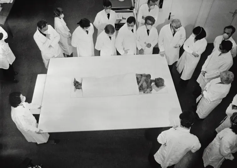 Photo d’époque, vue en plongée, de la momie entourée de savants en blouse blanche