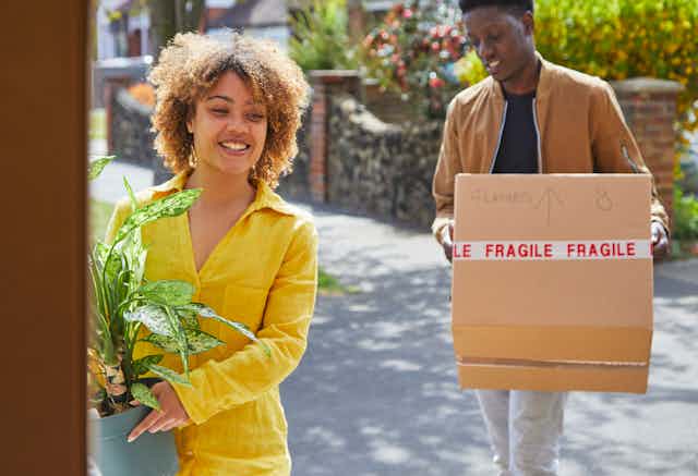 woman holding plant with man holding moving box