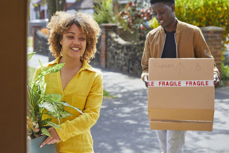 woman holding plant with man holding moving box
