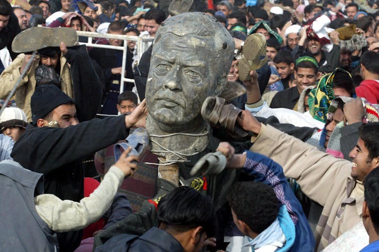 Iraqis crowd around the head from a statue of Saddam Hussein and some hit it with their shoes.