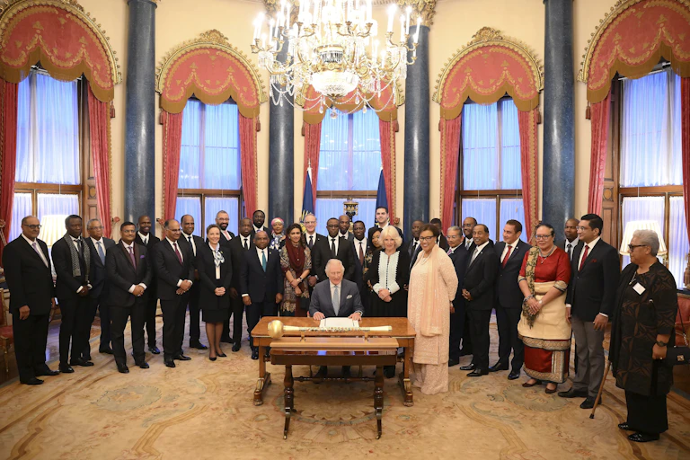A man seated behind a desk with other people standing behind him.