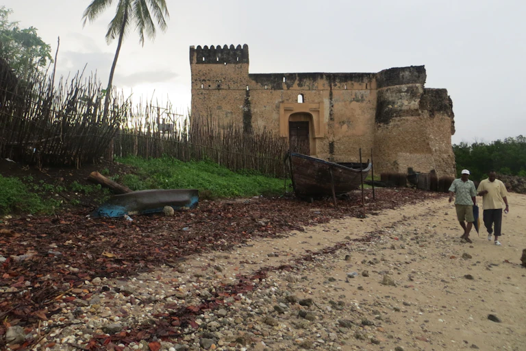 men walk on shore with stone ruin in background