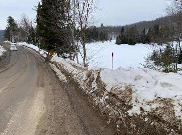A car drives down a clear road in the winter, with snowbanks on the side of the road