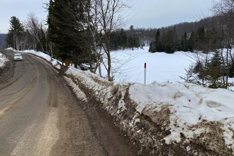 A car drives down a clear road in the winter, with snowbanks on the side of the road