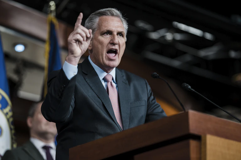 Standing behind a podium, a gray haired man speaks.