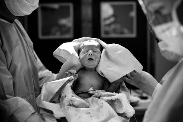 Black and white image of two health care providers holding a newborn