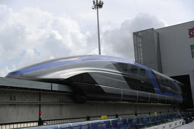 a futuristic train with a long tapered nose sits on a raised track
