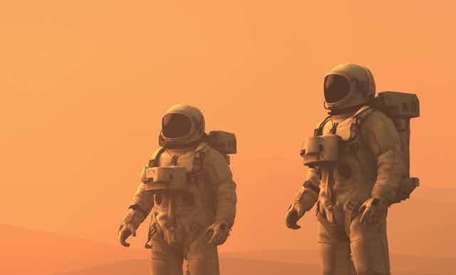 Against a dusky orange sky, two astronauts in white spacesuits walk a barren landscape.