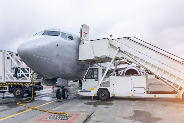 The nose of a parked plane with several vehicles next to it, along with a fuel hose snaking along the ground
