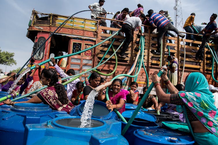 A group of people fill water in their drums from a truck carrying municipal water.