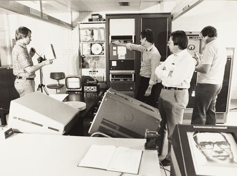A group of male scientists around an old computer.