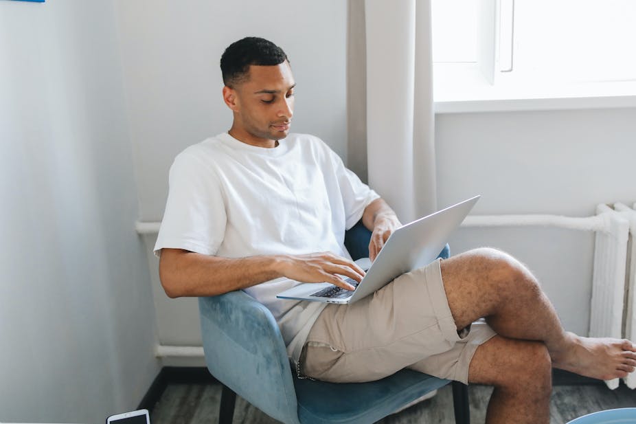 Man sitting in chair on laptop with legs crossed at the knee.