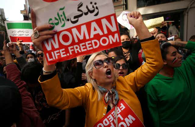 A group of women at a protest carrying signs that read: woman, life, freedom.