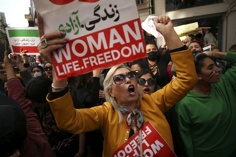 A group of women at a protest carrying signs that read: woman, life, freedom.