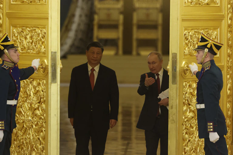 Two men gesture as they walk through golden doors opened by two men in uniform