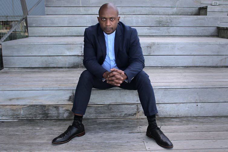 A Black man dressed in a dark suit is sitting on stairs made of stone.