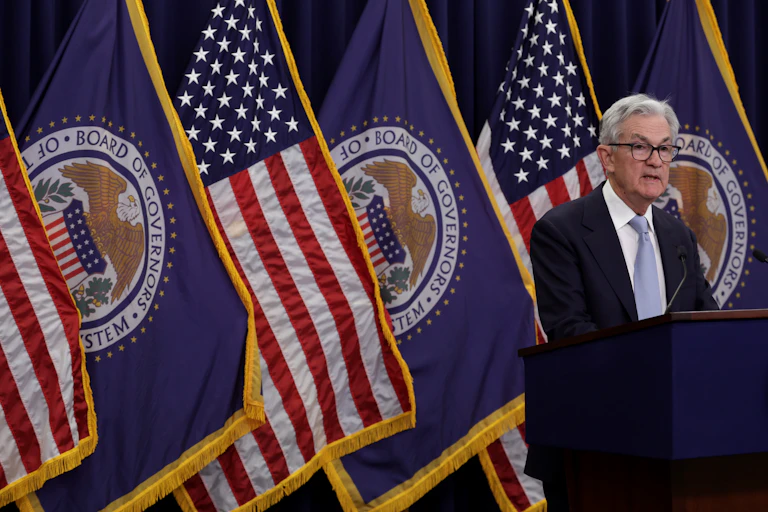 A man stands by a lectern in front of several US and Federal Reserve flags.