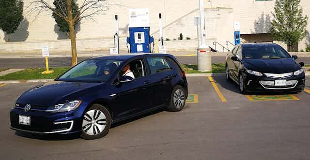 A person backs a navy blue car towards a charging station.