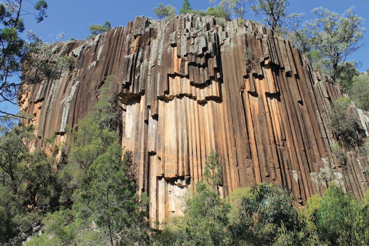 A towering pale brown coloured rock with vertical columns seemingly built into it