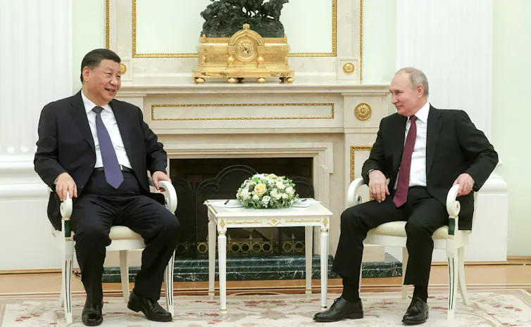 Two men wearing suits look at each other across a white table.