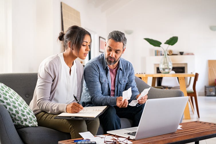 Couple calculating bills at home using laptop. Couple working on computer while calculating finances.