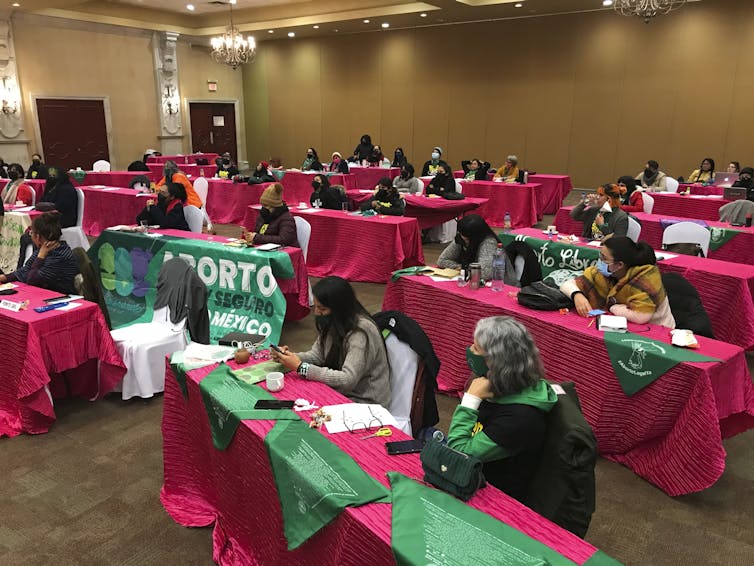 Women sit in a meeting room at long tables festooned with red and green tablecloths.