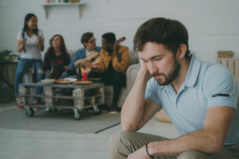 A man sits alone, while a group of other people talk loudly behind him.