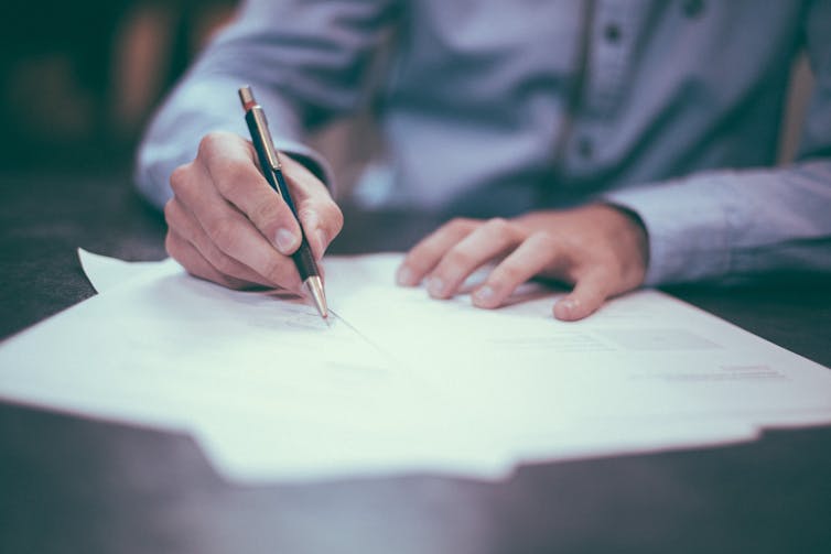 A man writes on a piece of paper using a ballpoint pen.