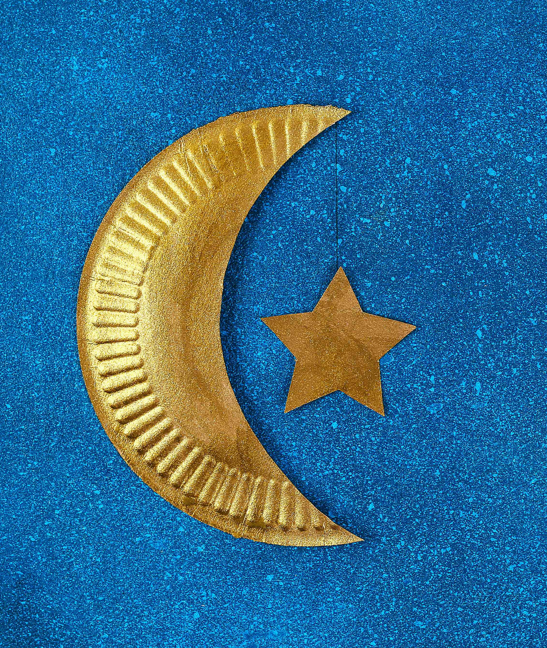 Paper cutout of a crescent moon and star are painted gold.