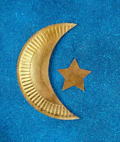 Paper cutout of a crescent moon and star are painted gold.