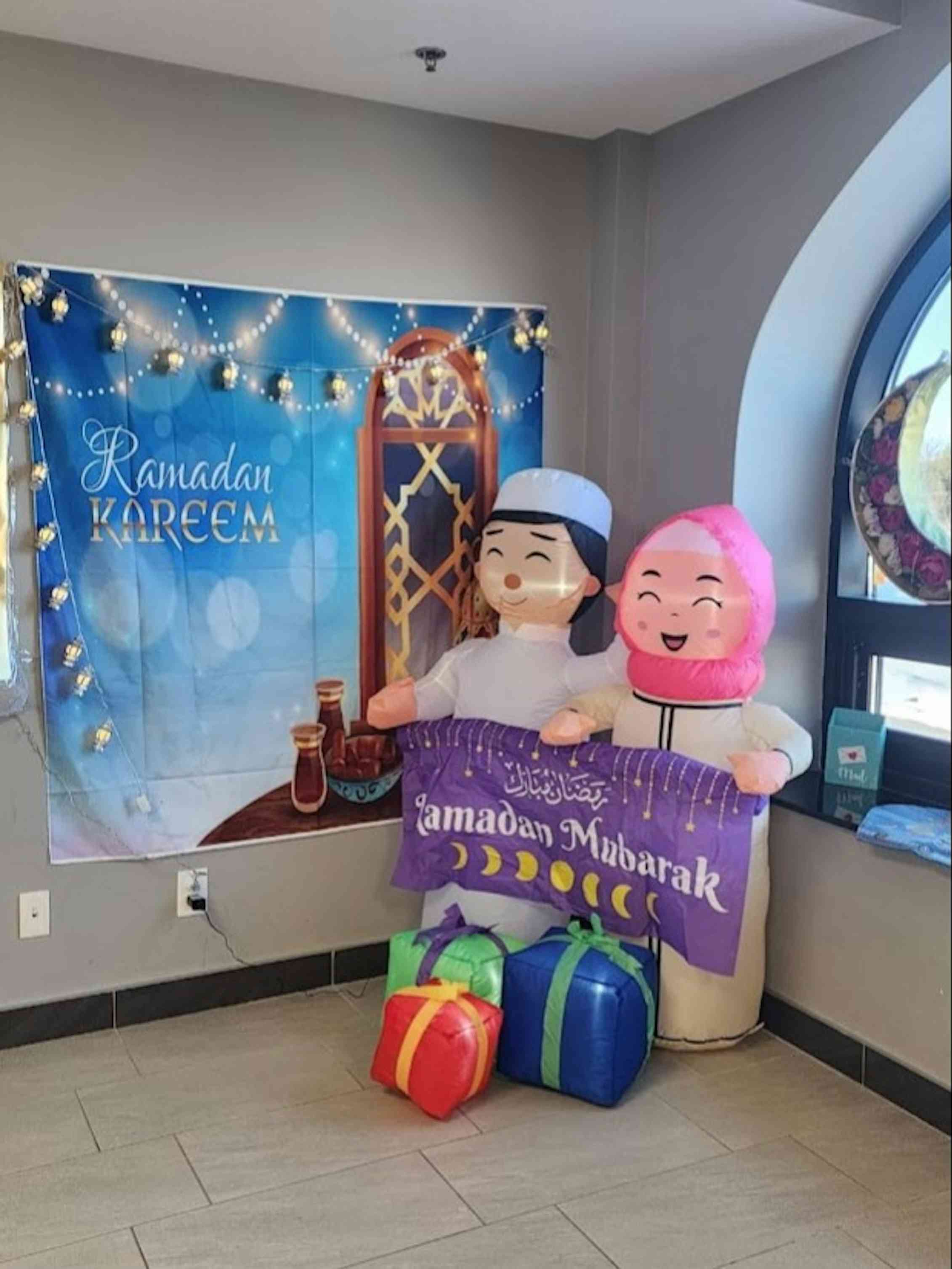 Decor seen in a school hallway of a sign saying 'Ramadan Kareem' with two smiling figures and presents in front of them.