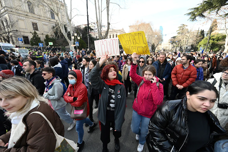 Large crowd of protesters, some holding signs in air, demonstrate outside Georgia's Parliament