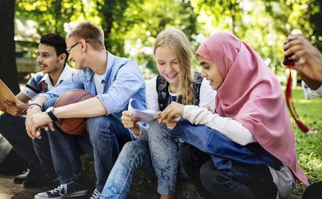 Students seen sitting outdoors looking at a paper together.
