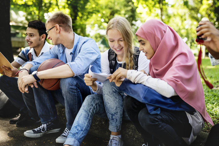Students seen sitting outdoors looking at a paper together.
