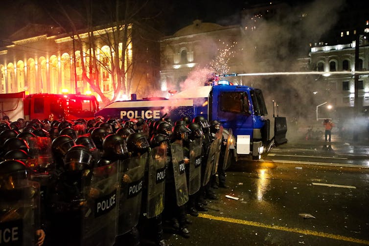 Police in riot gear form a barrier during a protest after dark