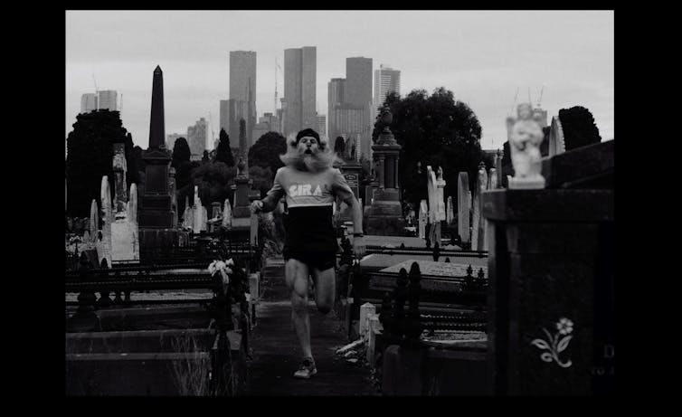 Black and white image. A man jogs in a graveyard.