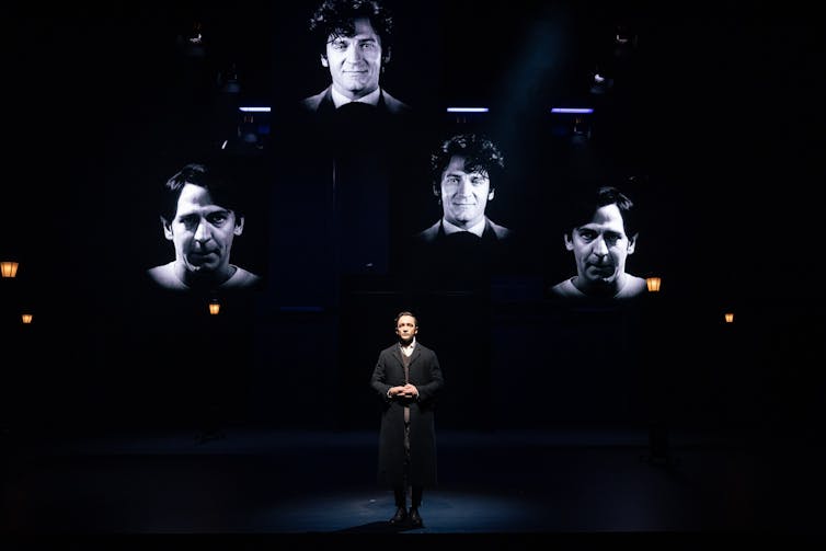 A man on stage, surrounded by screens.
