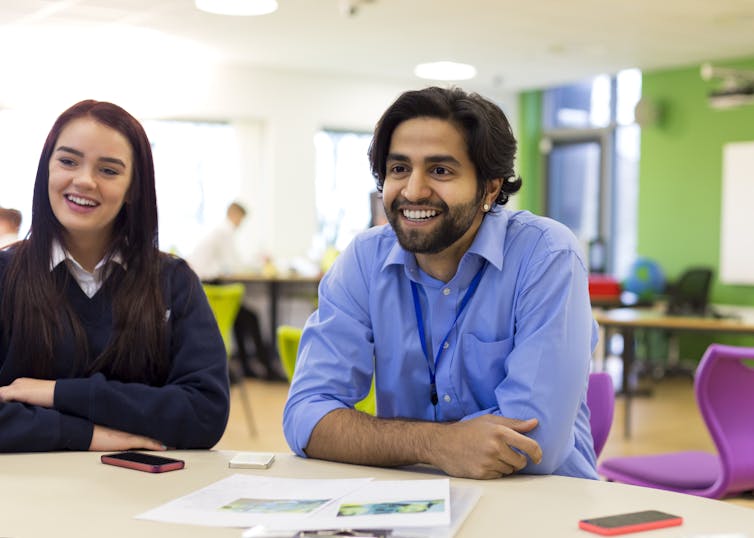 A teacher and a student sitting at a desk, smiling.