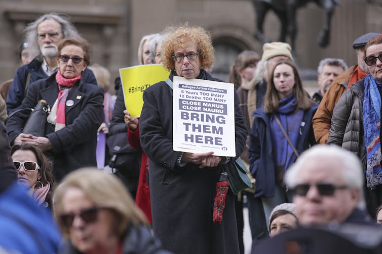 Woman holding placard at protest reading 'bring them here'