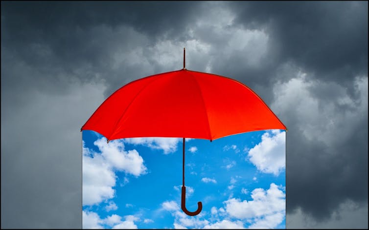 Red umbrella against gray stormy sky, with blue sky under the umbrella