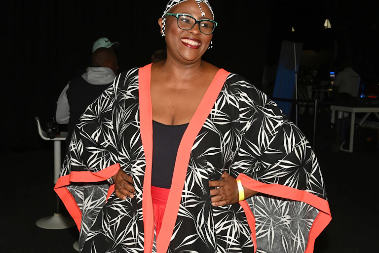 A woman smiles as she poses for a photo, wearing glasses, a beaded headpiece and a kimono-style outfit.