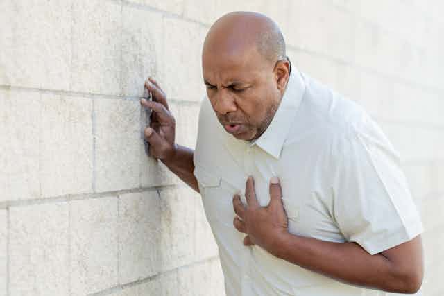 Man holding onto a wall and clutching his chest