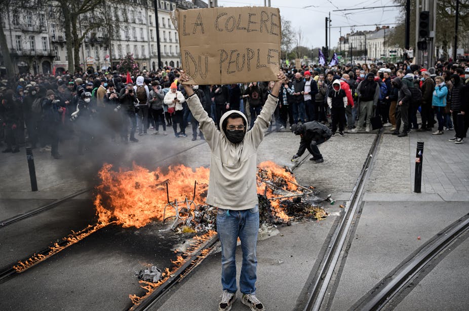Un manifestant debout à côté d'un feu dans la rue tient une pancarte sur laquelle on peut lire "La colère du peuple" alors que les manifestants font face à la police lors d'une manifestation dans le cadre d'une journée nationale de grèves et de protestations, à Nantes, le 23 mars 2023.