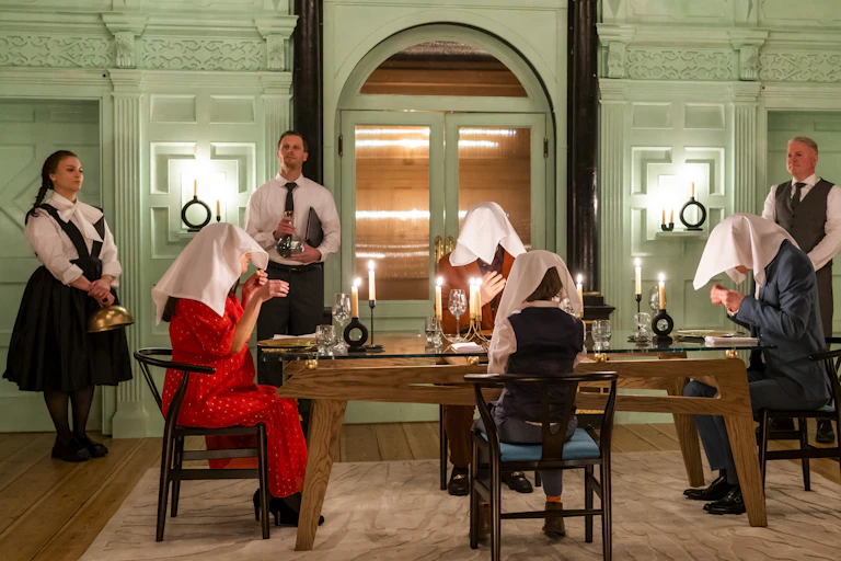 Four diners sit with napkins placed over their heads, with wait staff stood behind them.