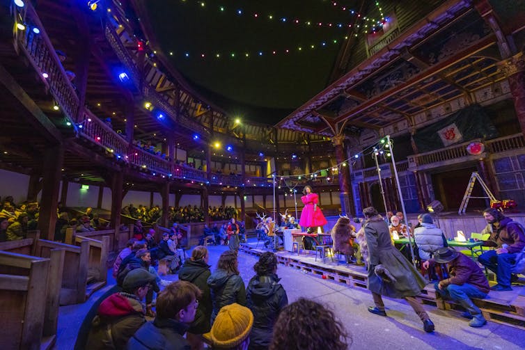 A fairylight strung outdoor theatre in the round with a large table at the centre.